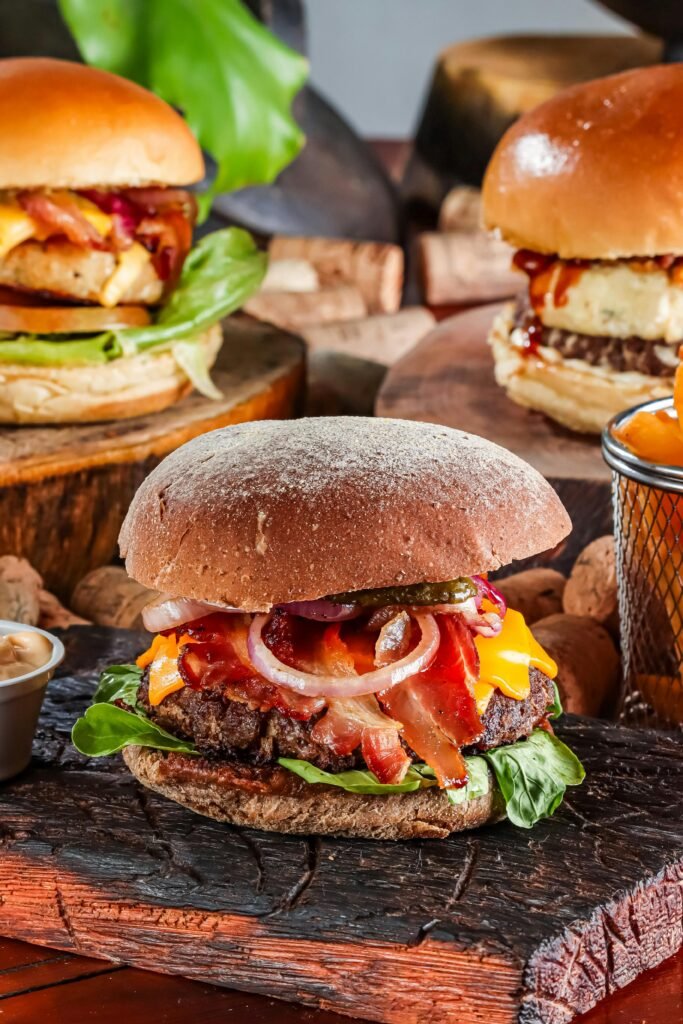 Close-up of gourmet burgers with cheddar, bacon, and vegetables on wooden boards.
